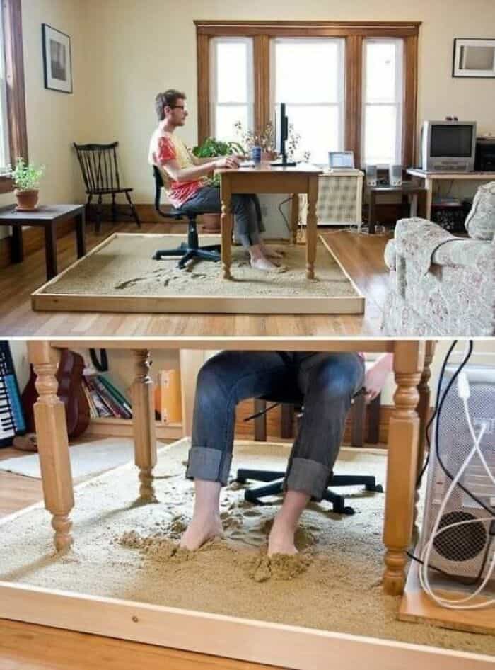 A person working at a desk in a cozy home office with large windows, a computer, and plants.