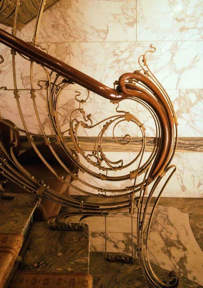 Elegant wrought iron staircase railing with intricate scrollwork and marble wall background.