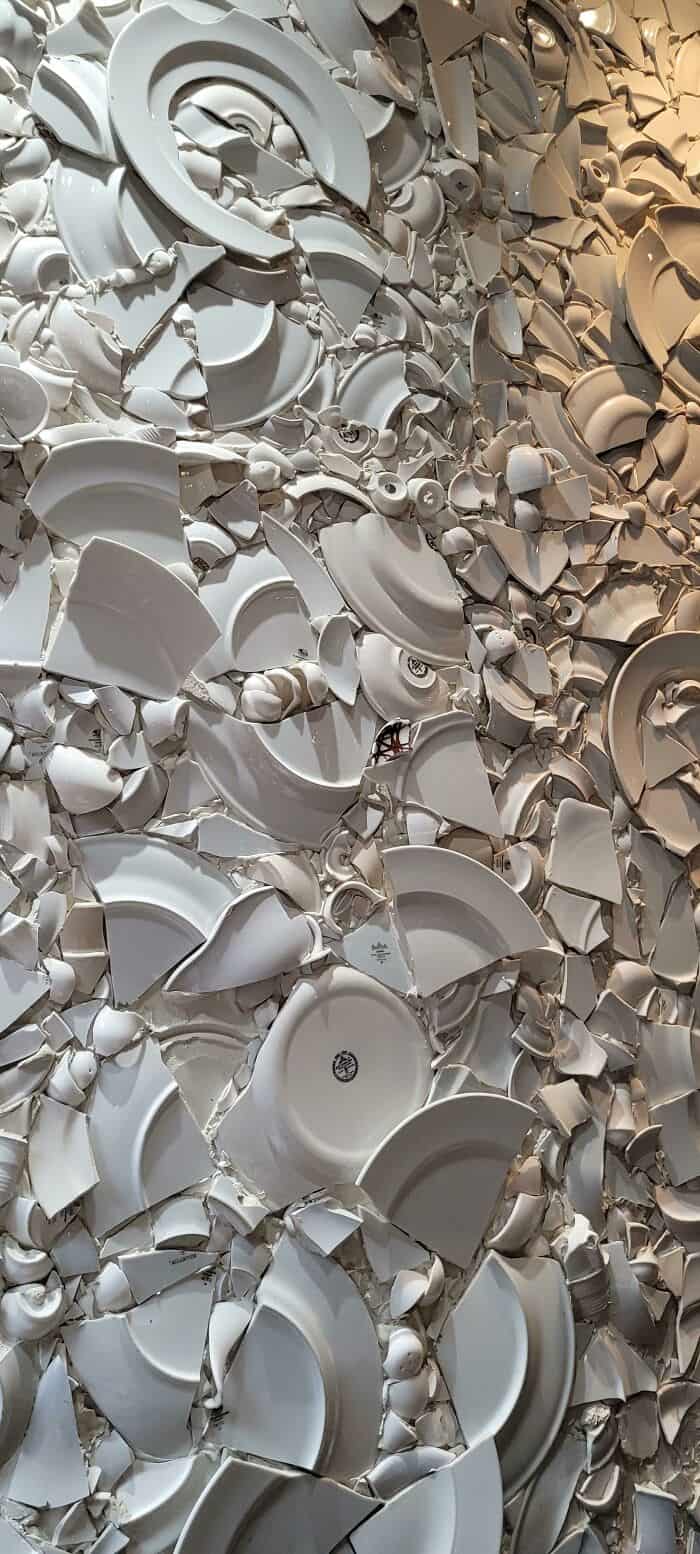 Abstract wall art made from broken white ceramic dishes and plates, creating a textured, artistic mo.