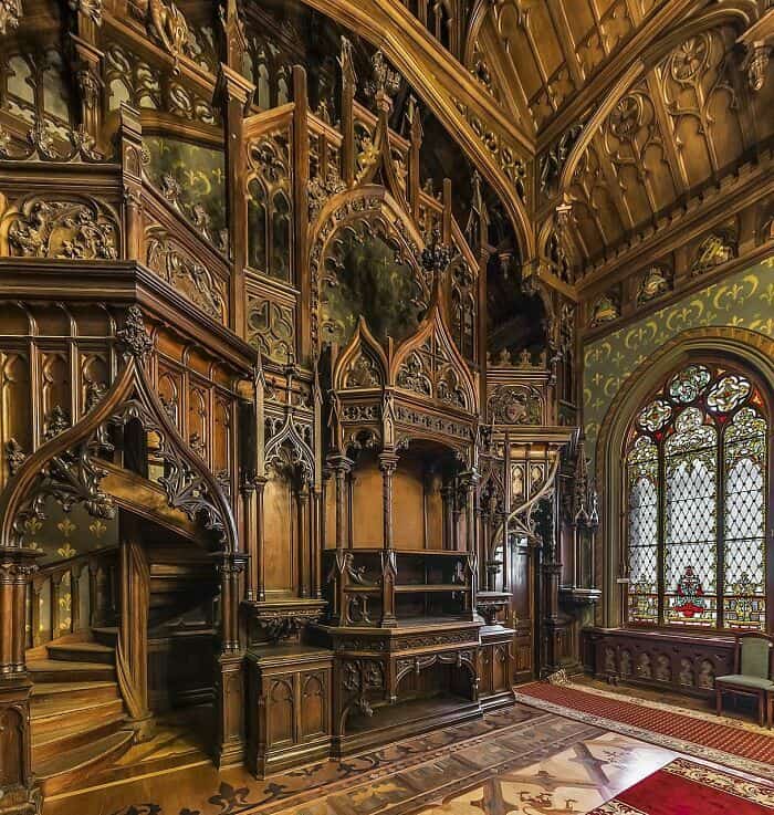 Gothic-style wooden interior featuring elaborate carvings, stained glass windows, and ornate archite.