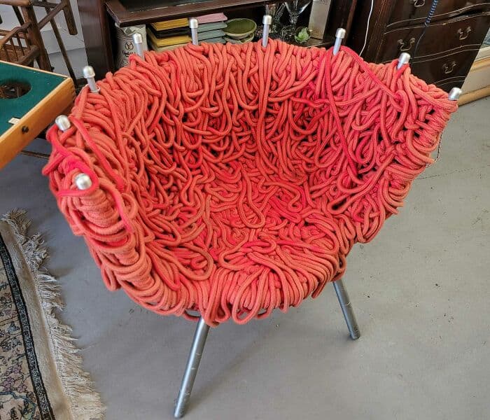 Yarn chair with a unique pleated design, resembling tangled fabric, supported by metal legs for a mo.