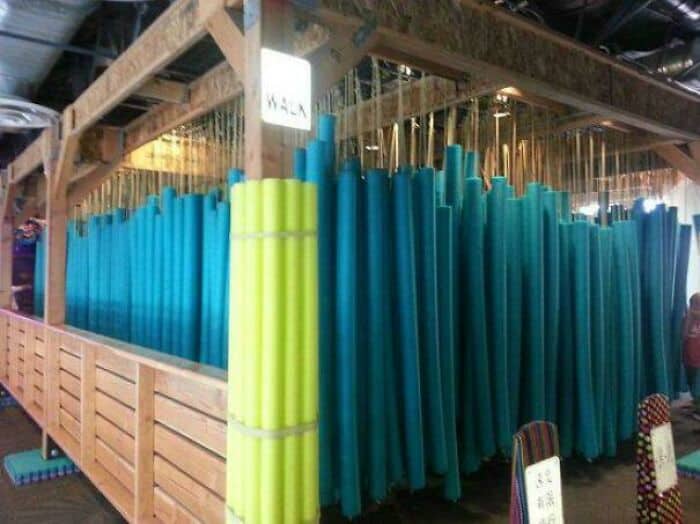 Bright blue and yellow pool noodles organized on a wooden rack at Pleated Jeans.