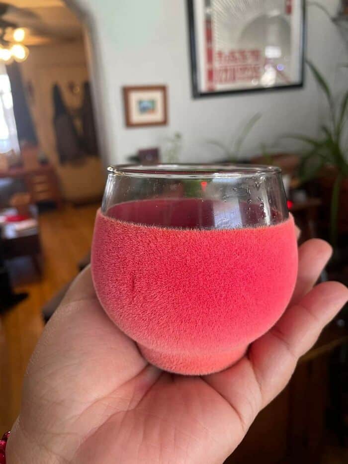 Pink frosted glass with a red candle inside, held in a person's hand in a cozy indoor setting.