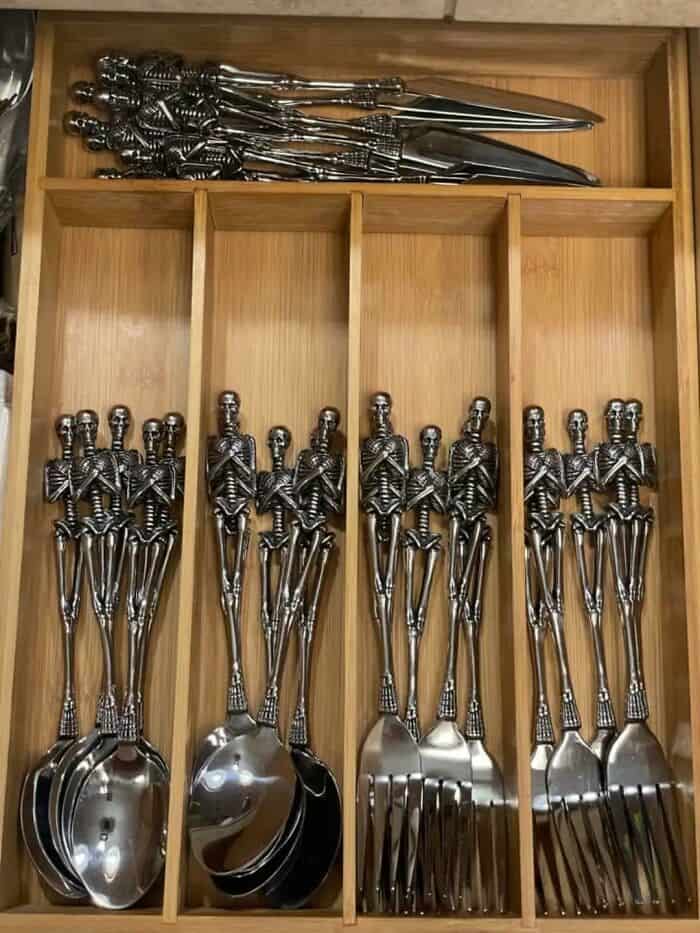 Skeleton-shaped utensils and spoons arranged in a wooden drawer for a quirky kitchen decor.