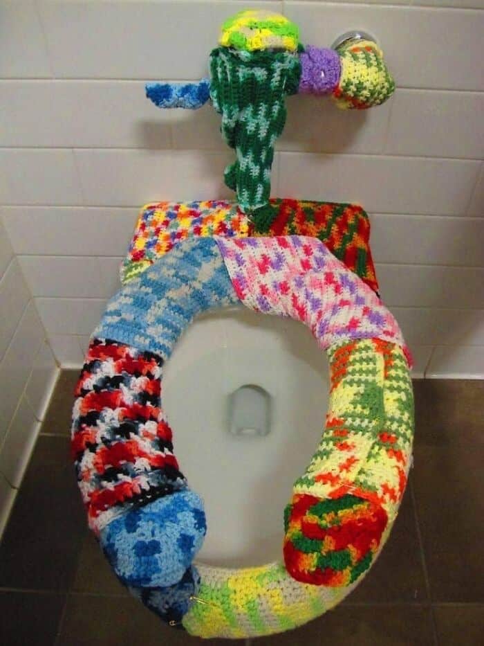 Colorful knitted toilet cover with matching flusher handle decoration.