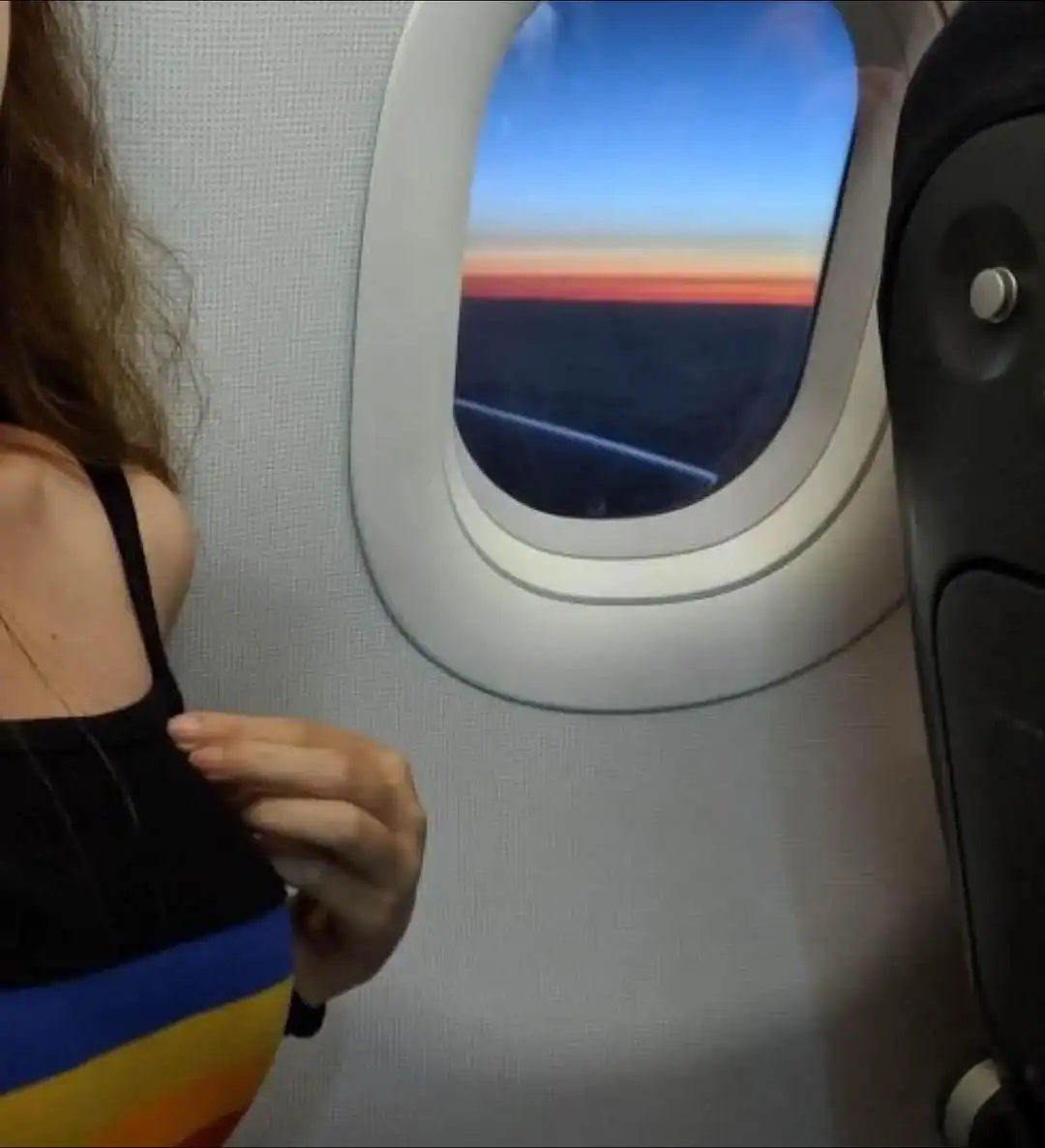 Sunset view from airplane window with a person adjusting their clothing.