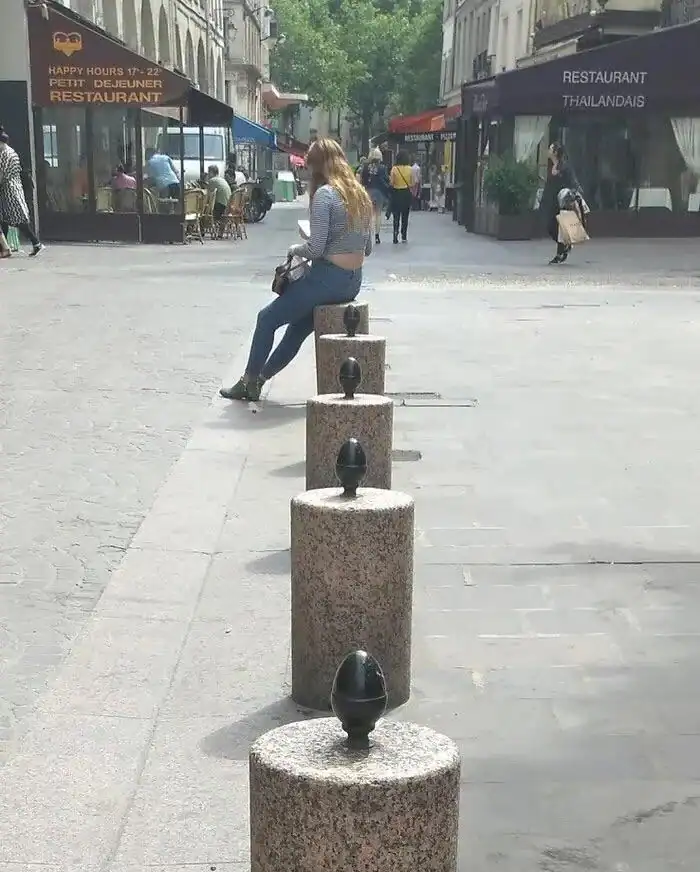 A woman sitting on a stone bollard in an urban shopping area.