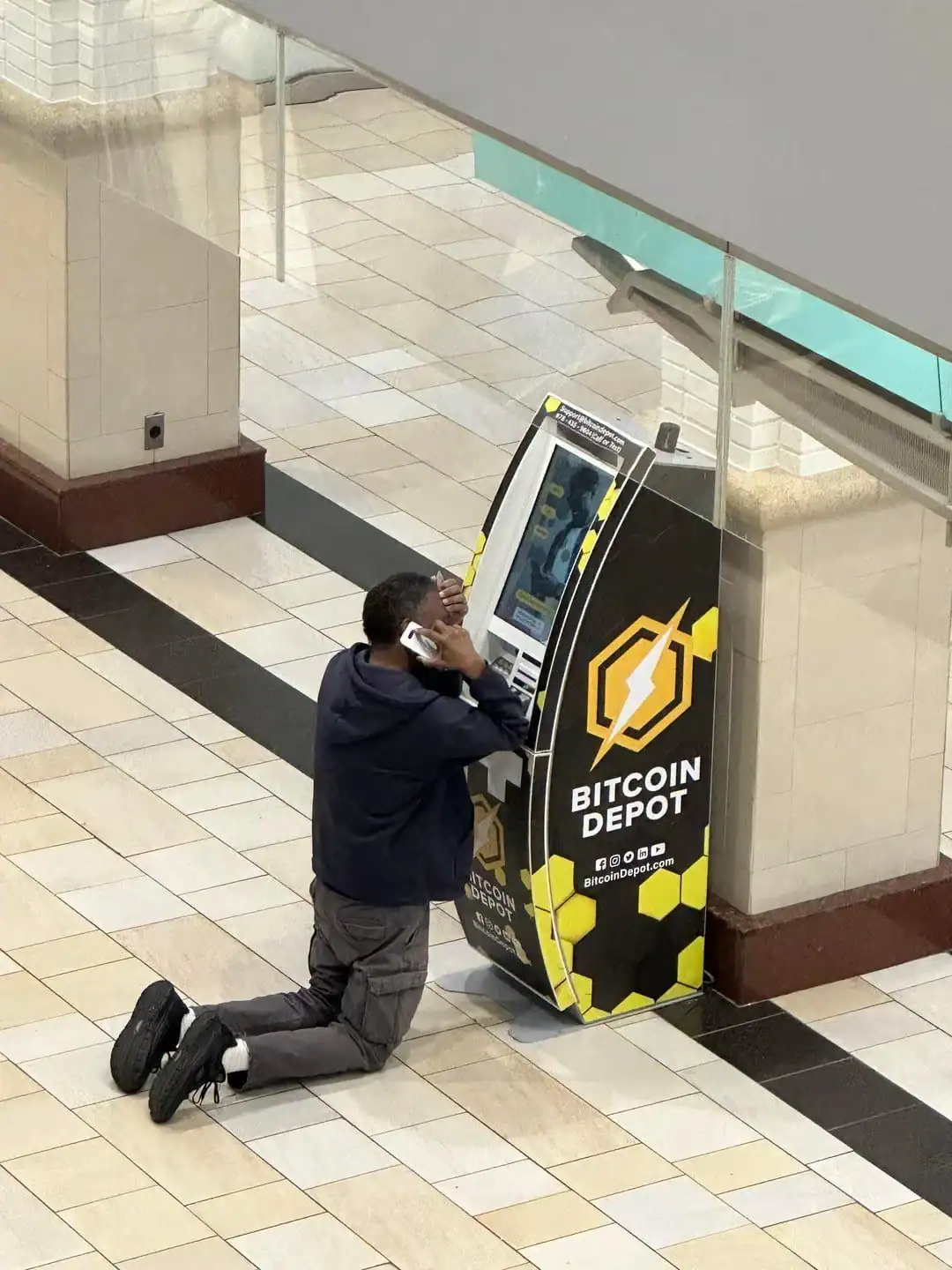 ATM machine with a Bitcoin logo, person kneeling and using the machine, shopping mall setting.