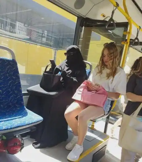 Woman in white top and pink skirt using phone on bus.