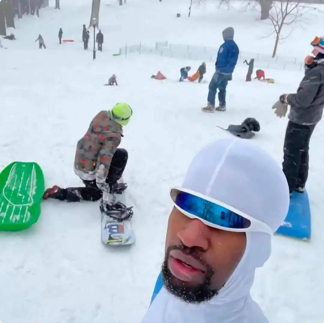 Snowboarding group in a snowy park, some people sitting and some standing with snowboards.