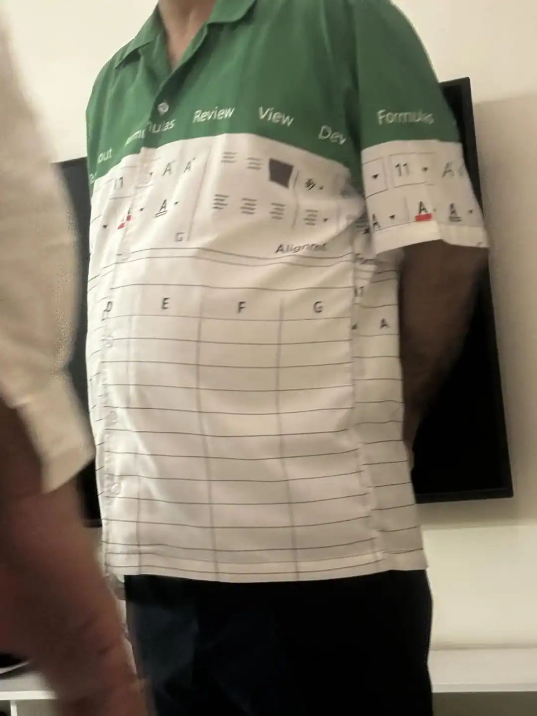 Person wearing a green and white shirt with text and diagrams, standing indoors.