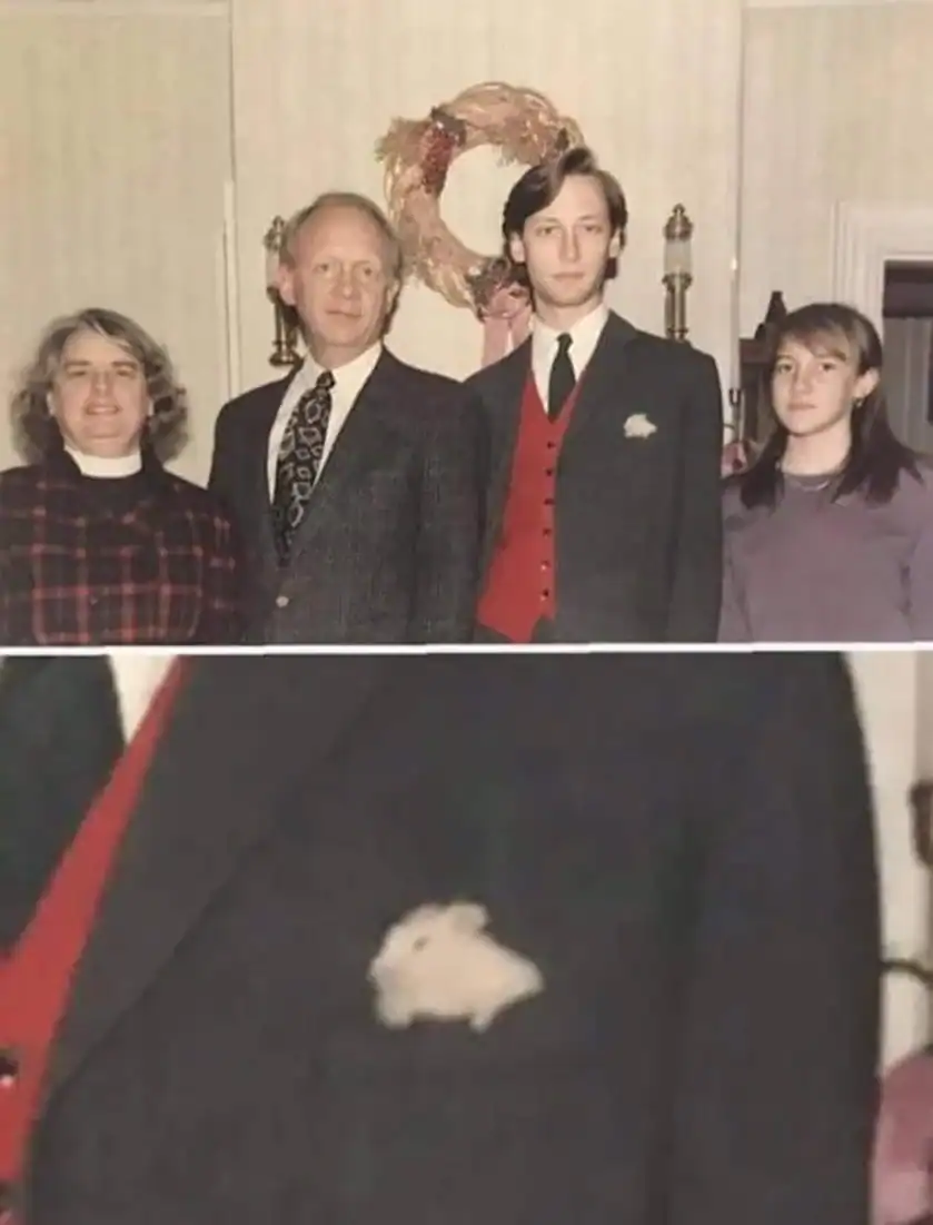Family portrait with four people, holiday wreath in background, and a small white animal on coat.