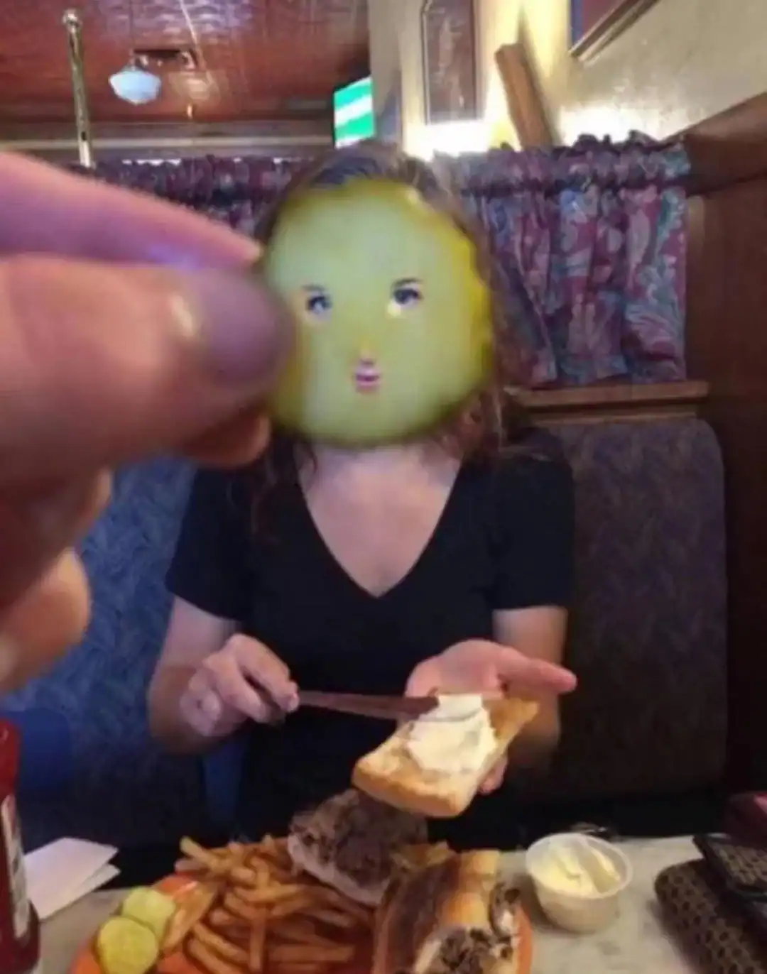 A woman with a face mask that looks like a yellow fruit, sitting at a table with food.