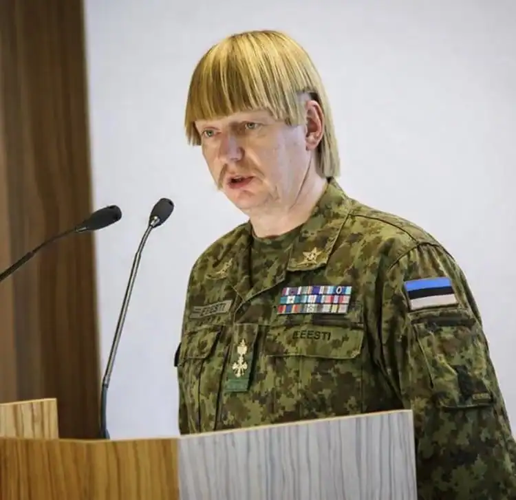 ESTONIAN military officer speaking at a podium with microphones, wearing camouflage uniform with med.