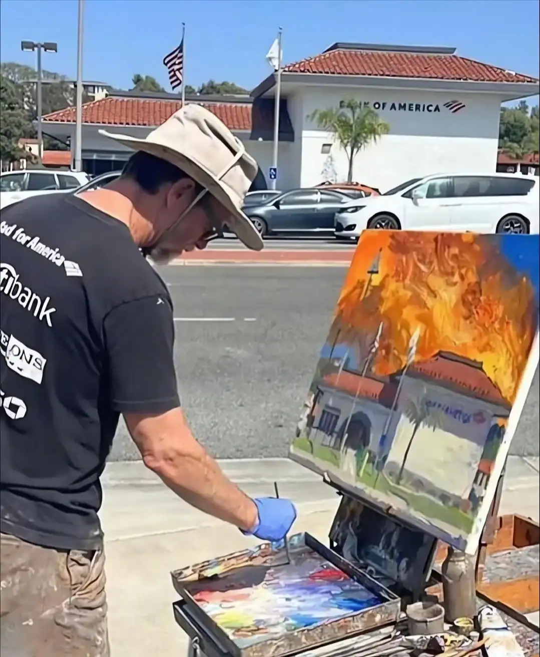 A man painting outdoors with a colorful fiery scene on canvas.