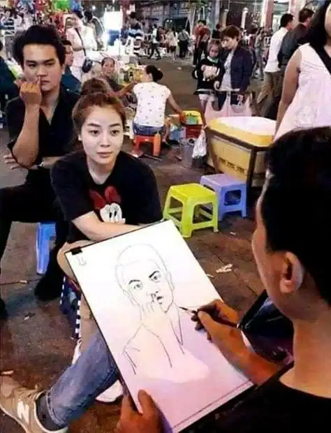 Artist drawing a portrait of a woman at a busy outdoor market.