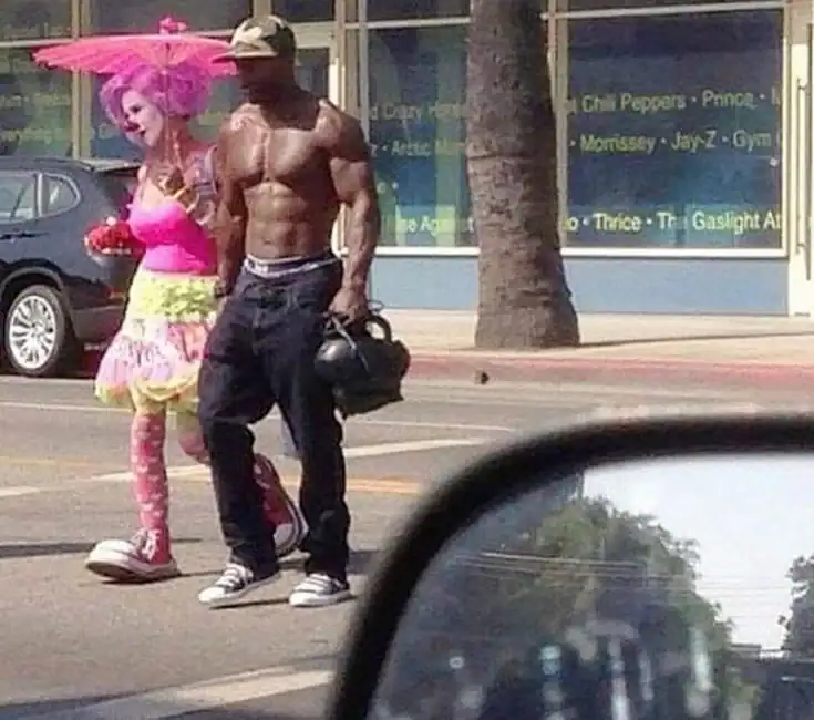Man and woman dressed as a clown and a shirtless man walking on the street.