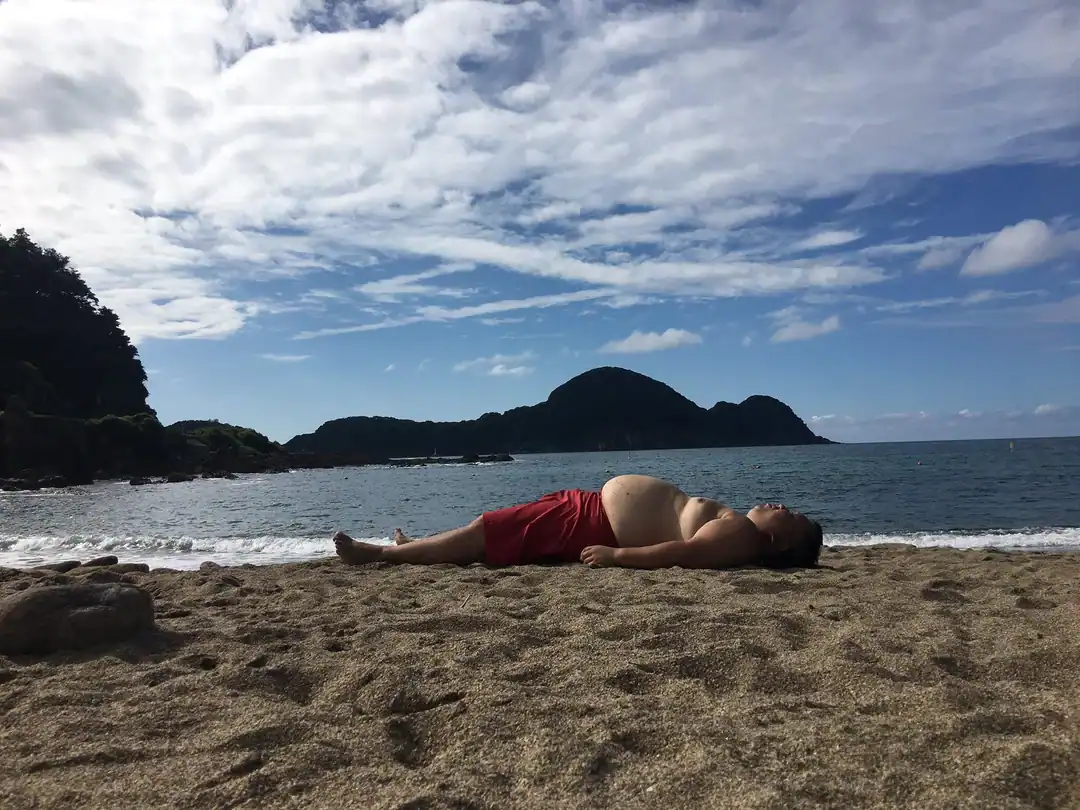 Relaxing woman lying on the beach with mountains and ocean in the background.