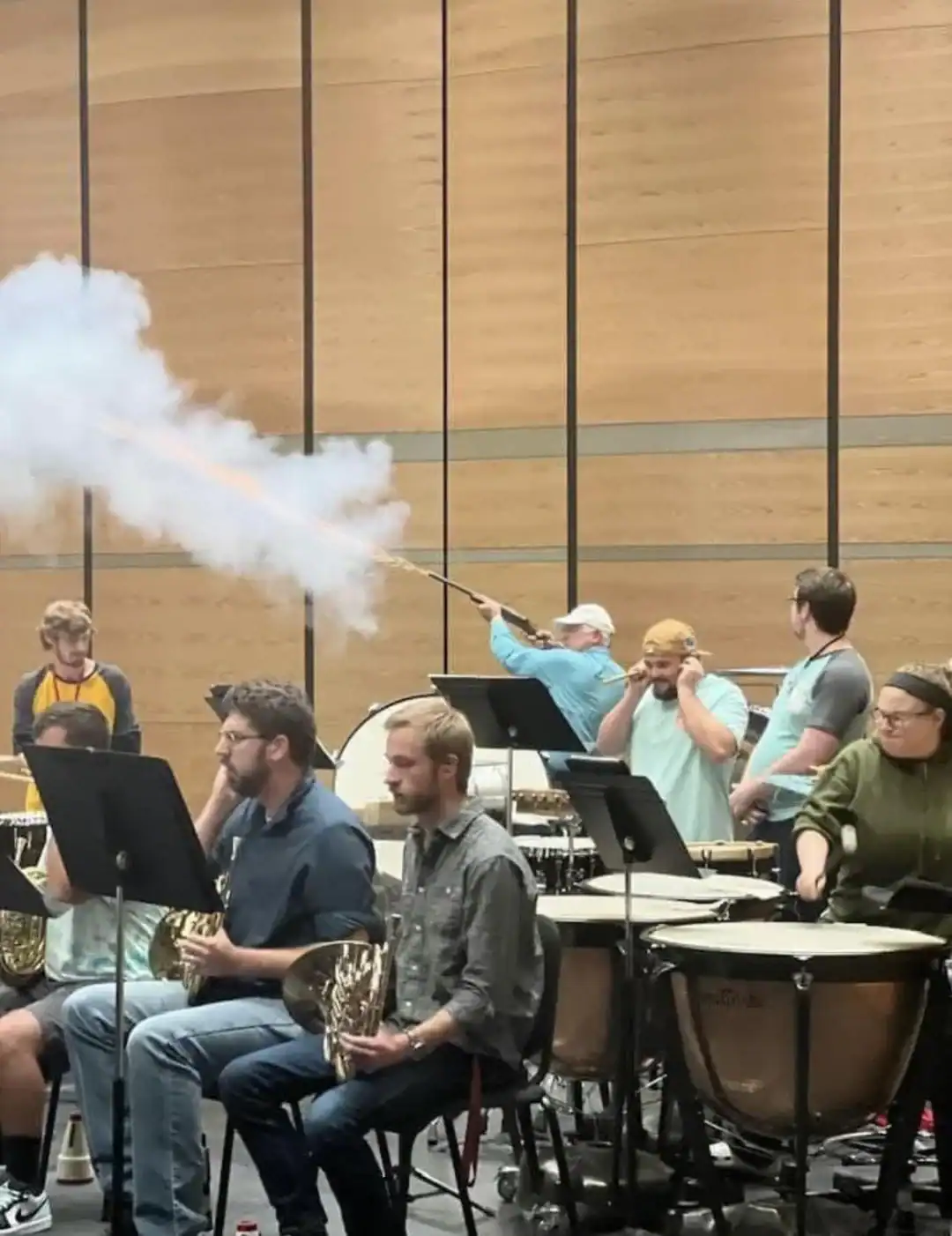 Musicians in a rehearsal room with a person spraying smoke from a stick.