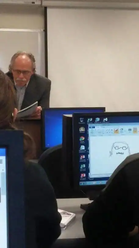 A man with glasses and gray hair reading a paper in a classroom setting.