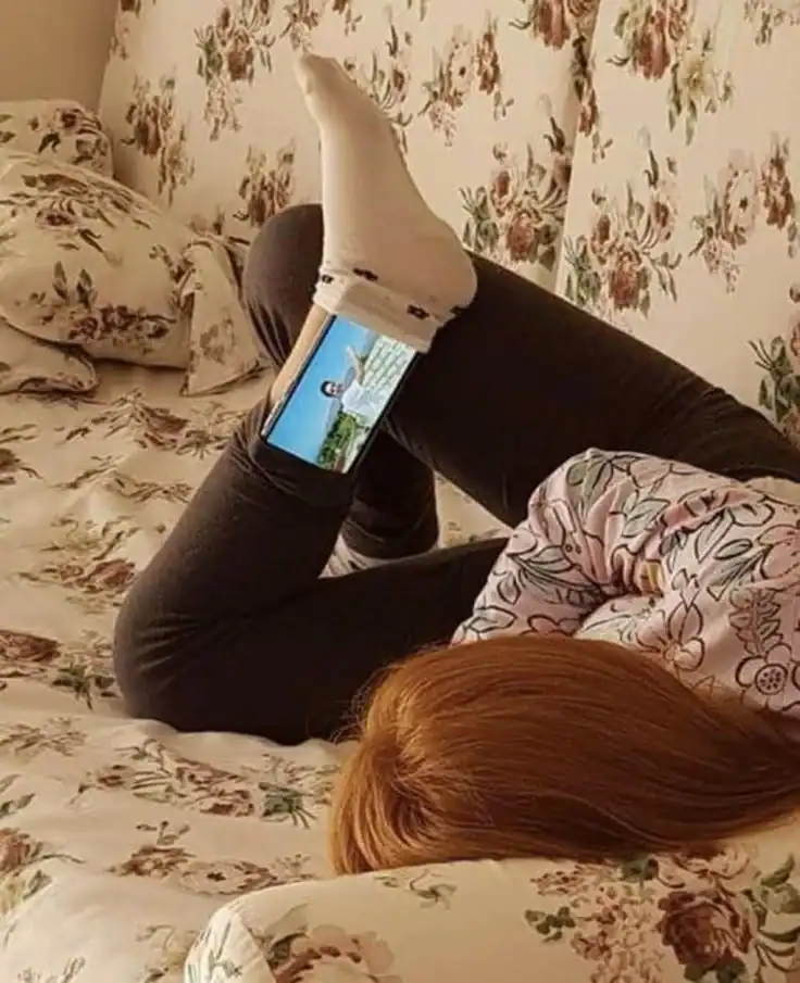 Person lying on bed with legs raised, wearing socks and floral pajamas.