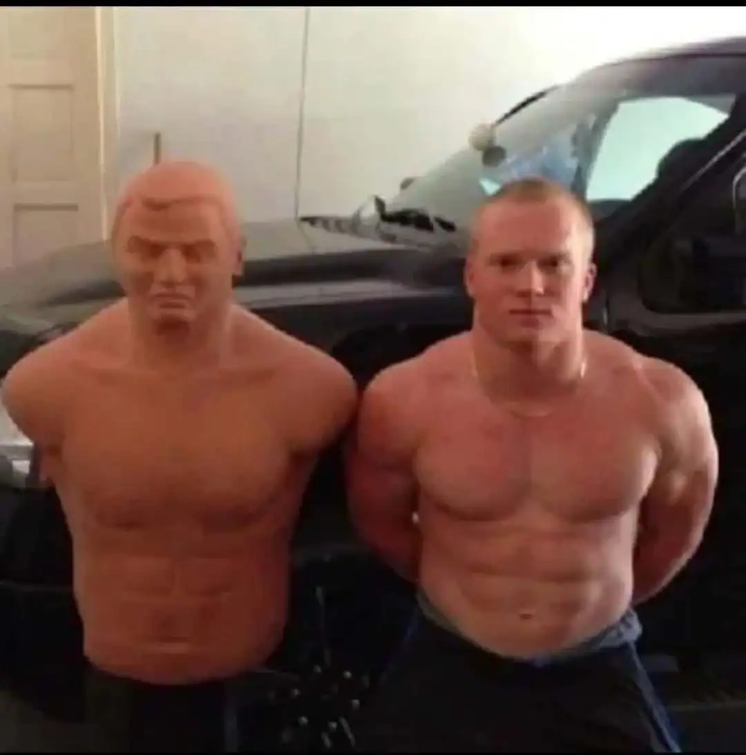 Man with muscular build standing next to a wax figure of a muscular man with pink hair.