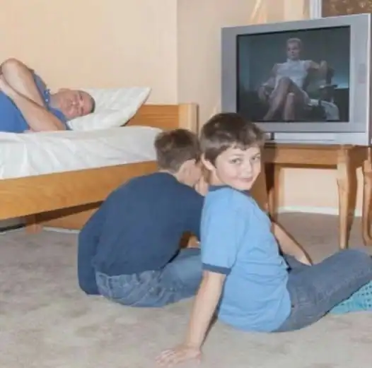 Two boys watching TV while an elderly person sleeps in the background.