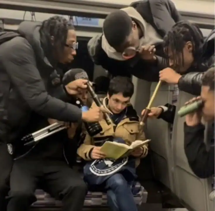 Group of young people surrounding a boy reading a book on a train.