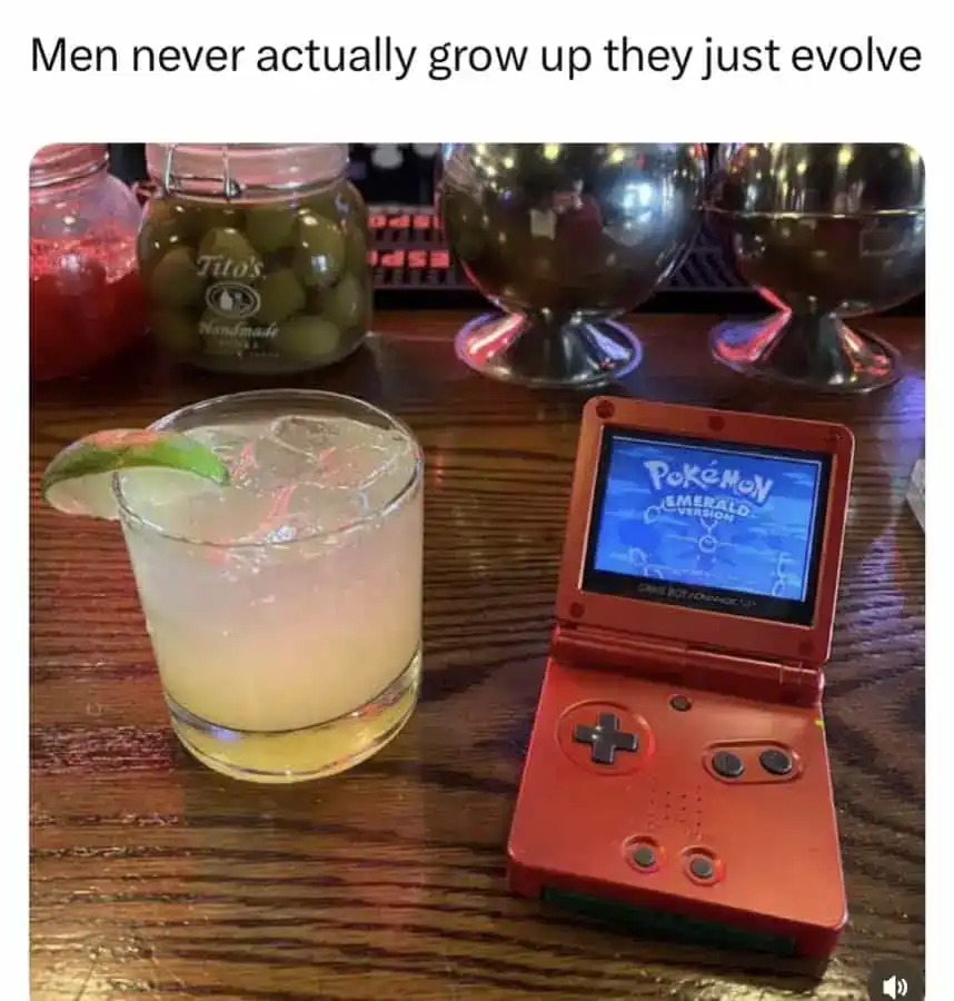 Red Pokémon Game Boy and cocktail on wooden bar counter with olives and metallic decor.