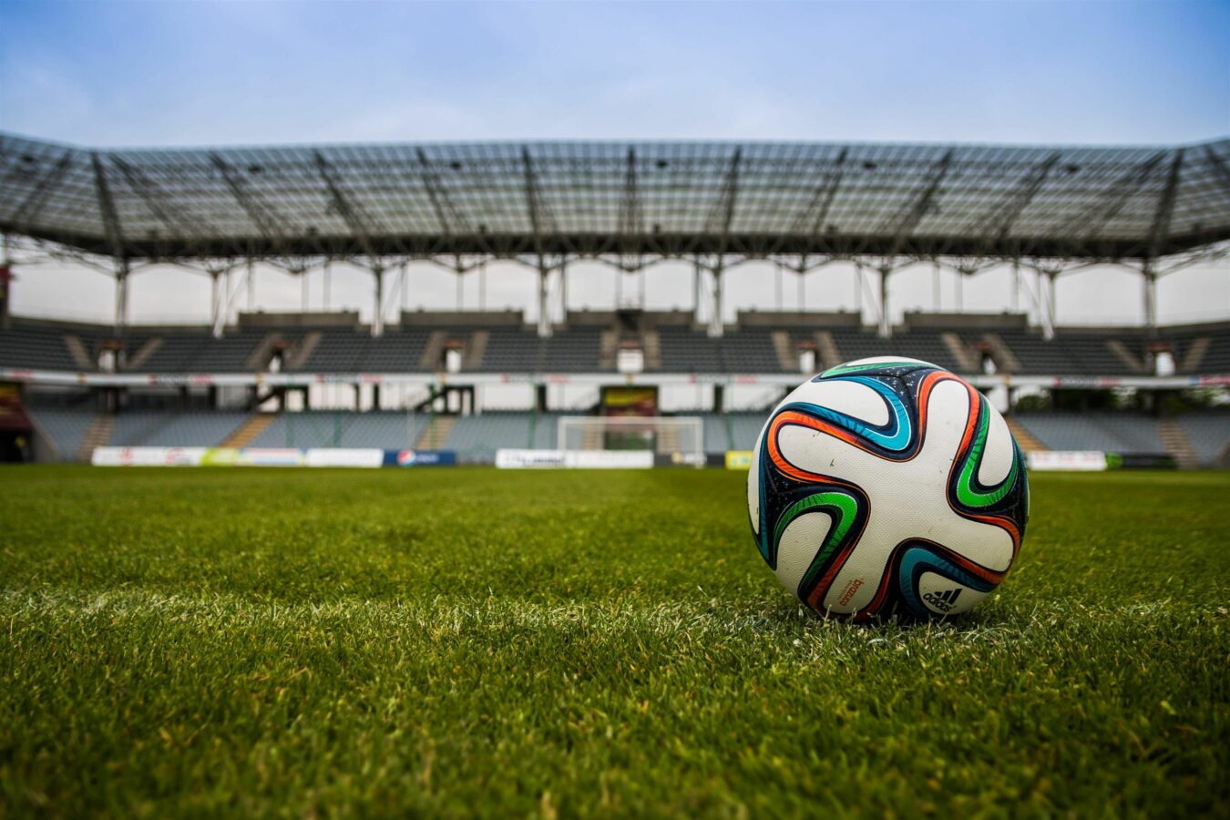 Soccer ball on field in empty stadium during daytime.