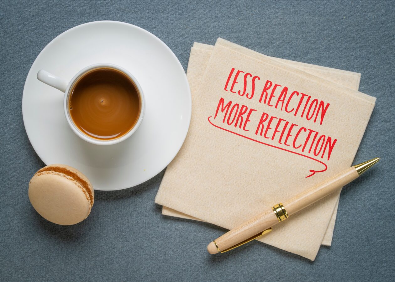 LESS REACTION MORE REFLECTION - Notepad with handwritten message, coffee cup, and macaron on a blue.