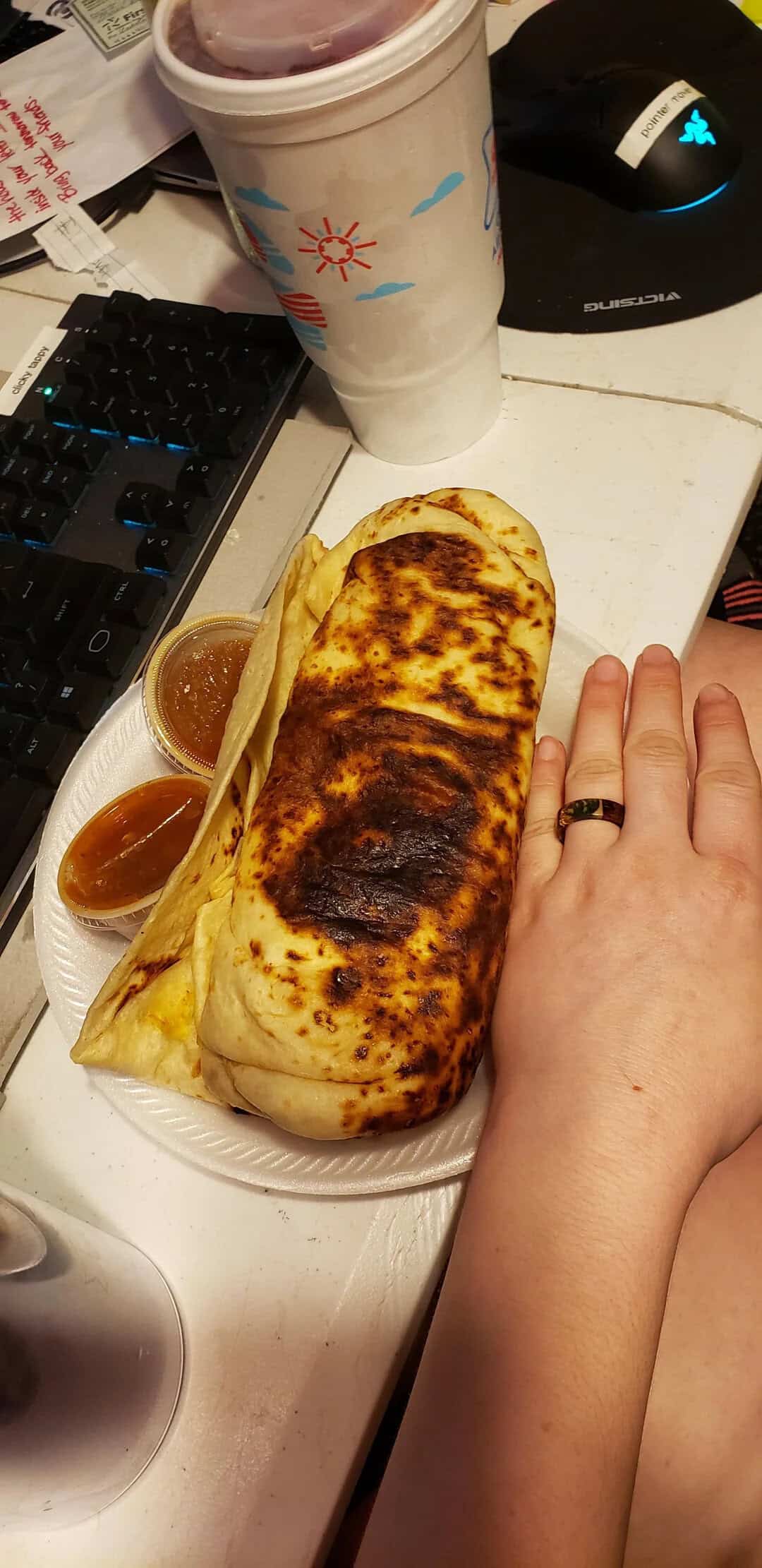 Large burrito with charred top, served with two sauces, on a white plate.