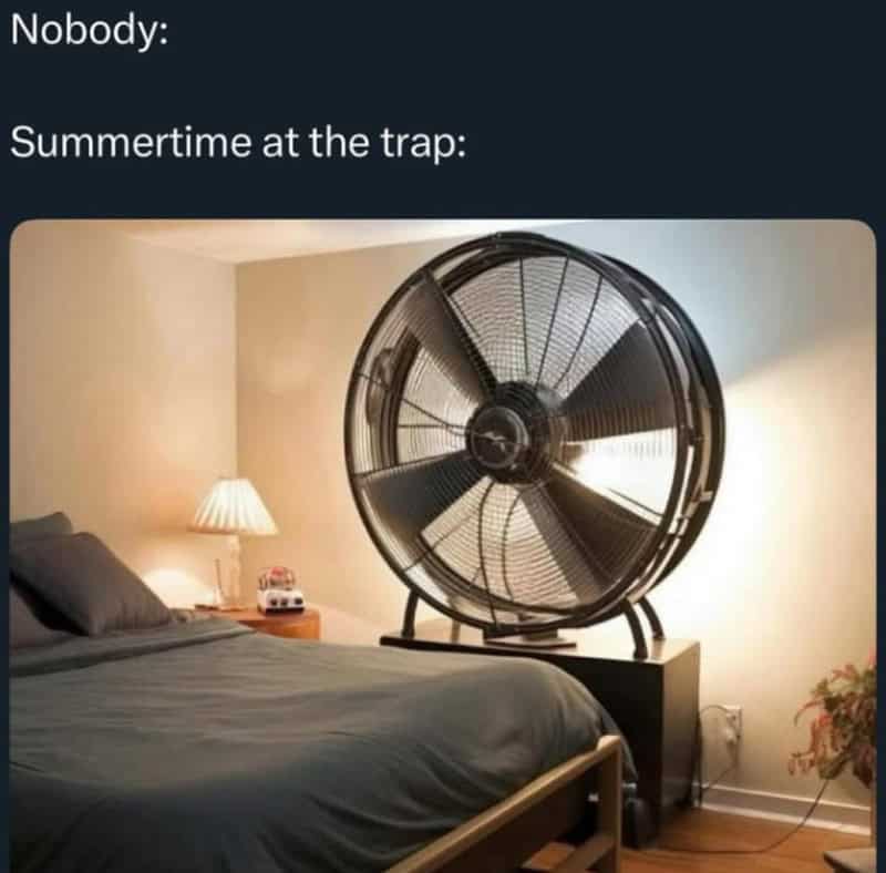 A large fan on a bedside table in a bedroom with a bed and lamp.