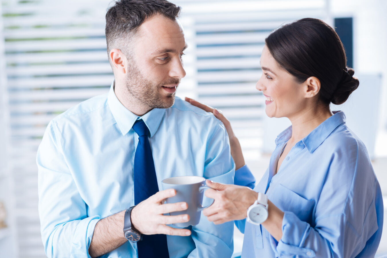 A woman and a man sharing a coffee, smiling and engaging in conversation in an office setting.