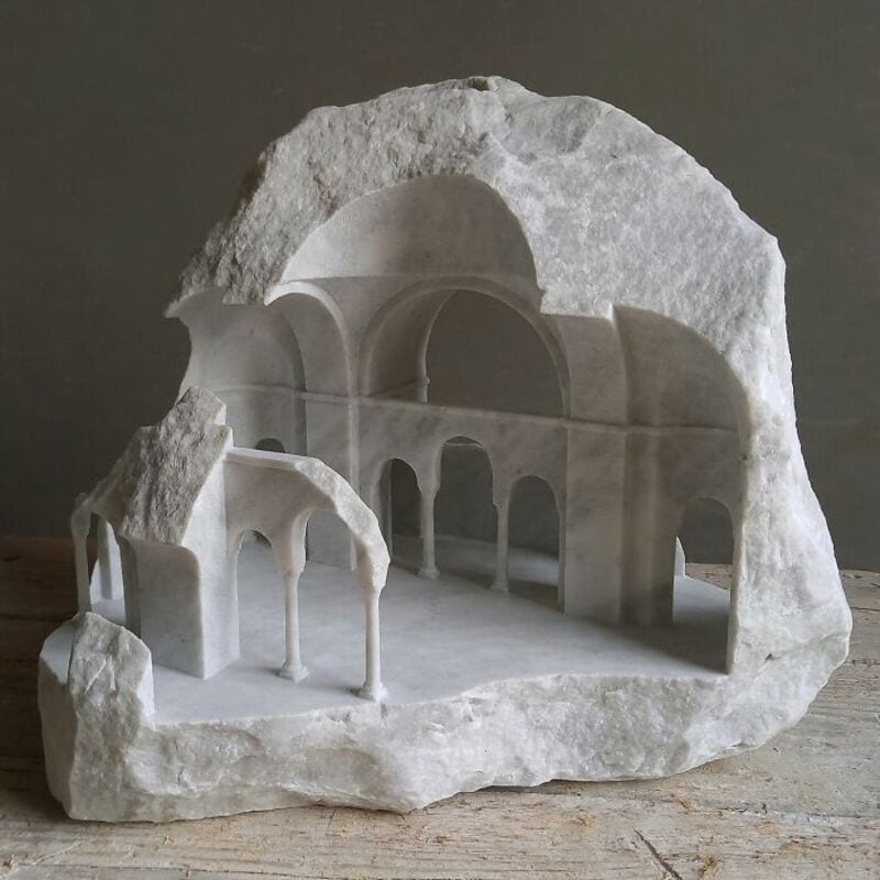 Marble sculpture of classical architecture with arches and columns on a rough stone base.