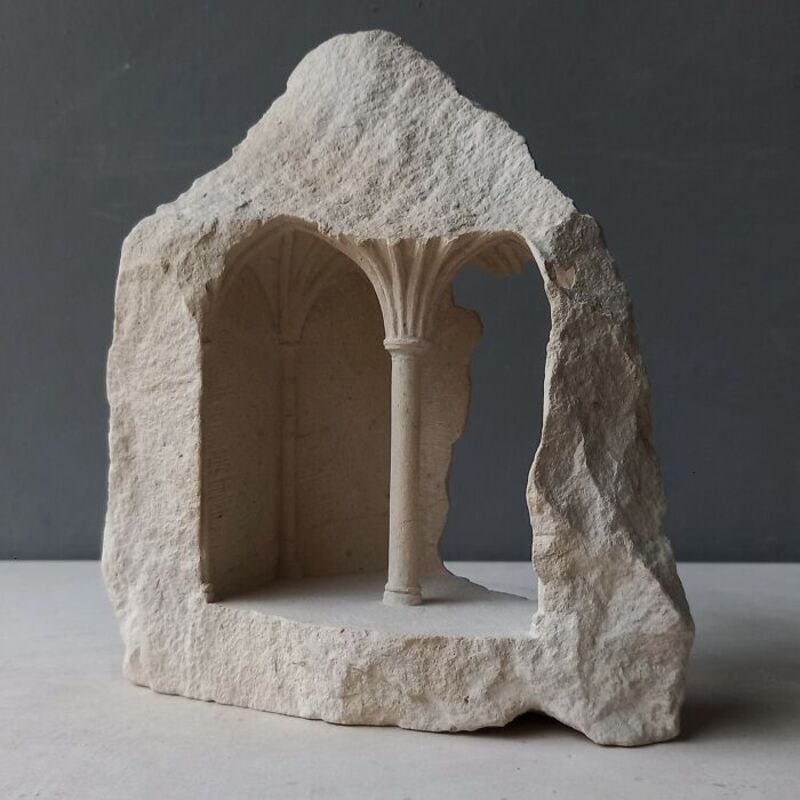 Marble sculpture of a small classical architectural structure with columns inside a rough stone.