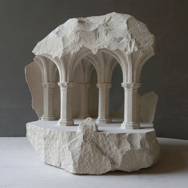 Marble sculpture of classical arches and columns with a rough stone top.