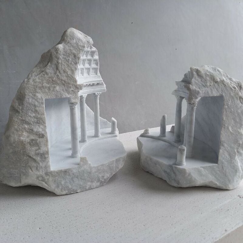 Two marble sculptures of classical architecture with columns and arches on a white surface.