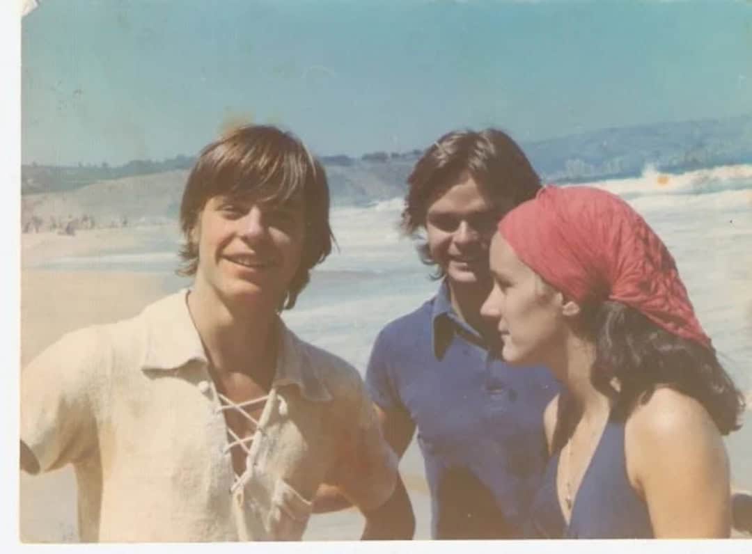 Three young people on the beach, smiling, with ocean and sky in the background.