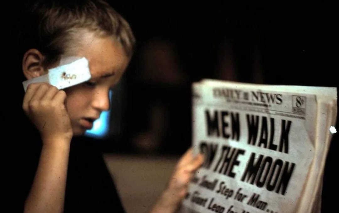 Young boy with a bandage on his face reading a newspaper titled 'Men Walk on the Moon'.