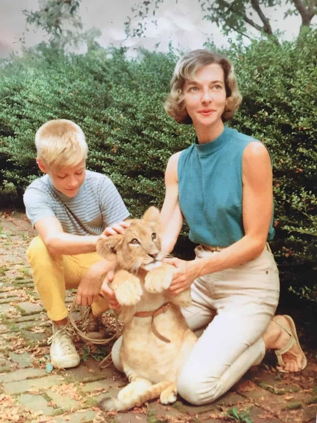 A woman and boy with a lion cub outdoors, woman in blue top, boy in striped shirt.
