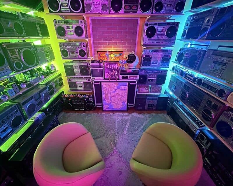 Room with colorful neon lights and numerous vintage boomboxes and radios on shelves.