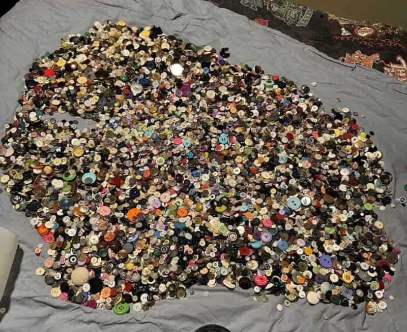 A large collection of various buttons spread out on a gray fabric surface.