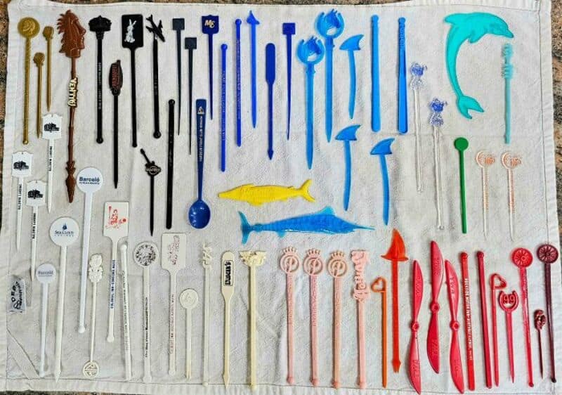 Collection of colorful plastic and metal stir sticks with various shapes and designs.