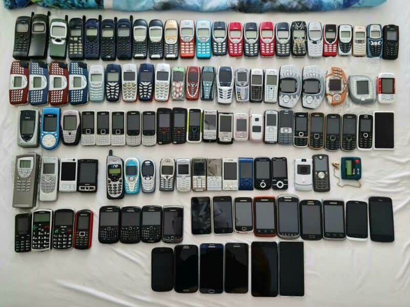 Collection of various old and new mobile phones arranged on a white surface.