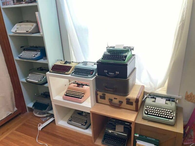 Collection of vintage typewriters on shelves and tables in a room.