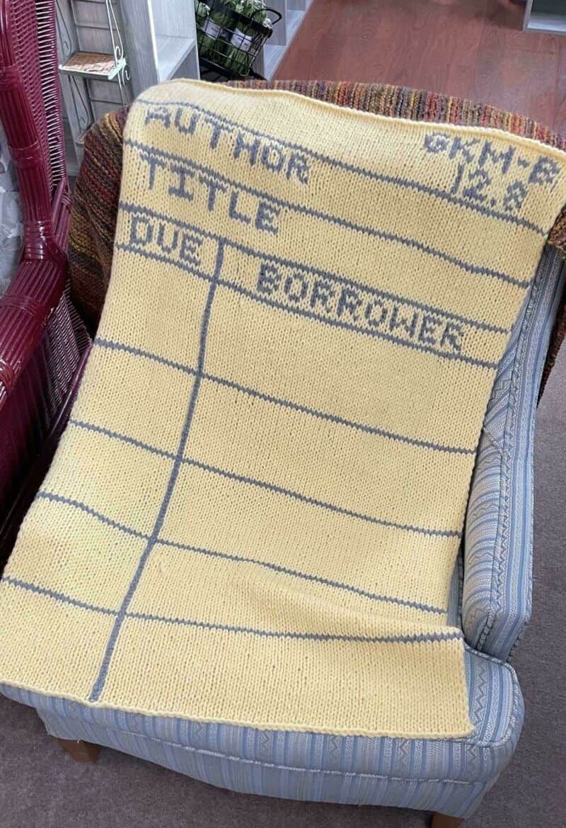 AUNT HOUR TICKET DUE FORMALITY written on a yellow knitted blanket draped over a chair.