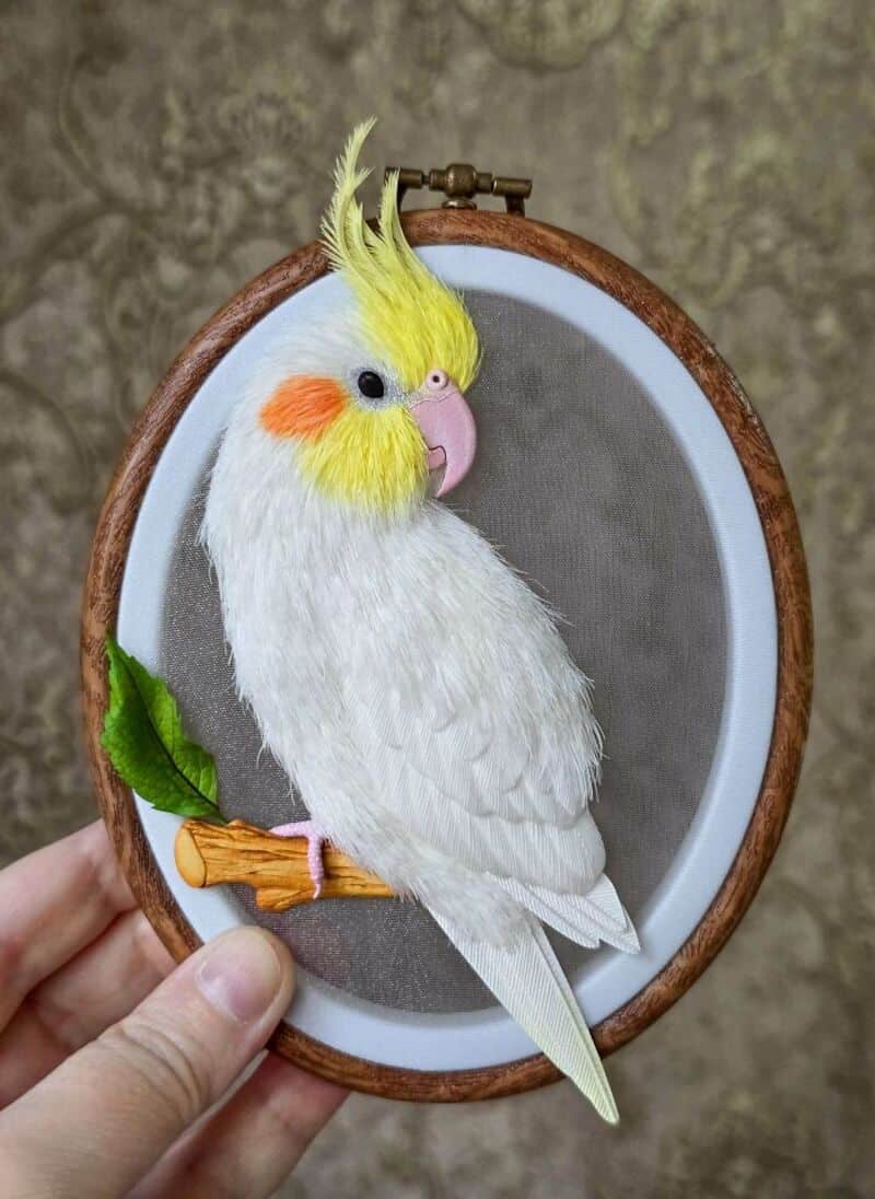 A colorful cockatoo plush toy with a yellow crest inside an embroidery hoop.