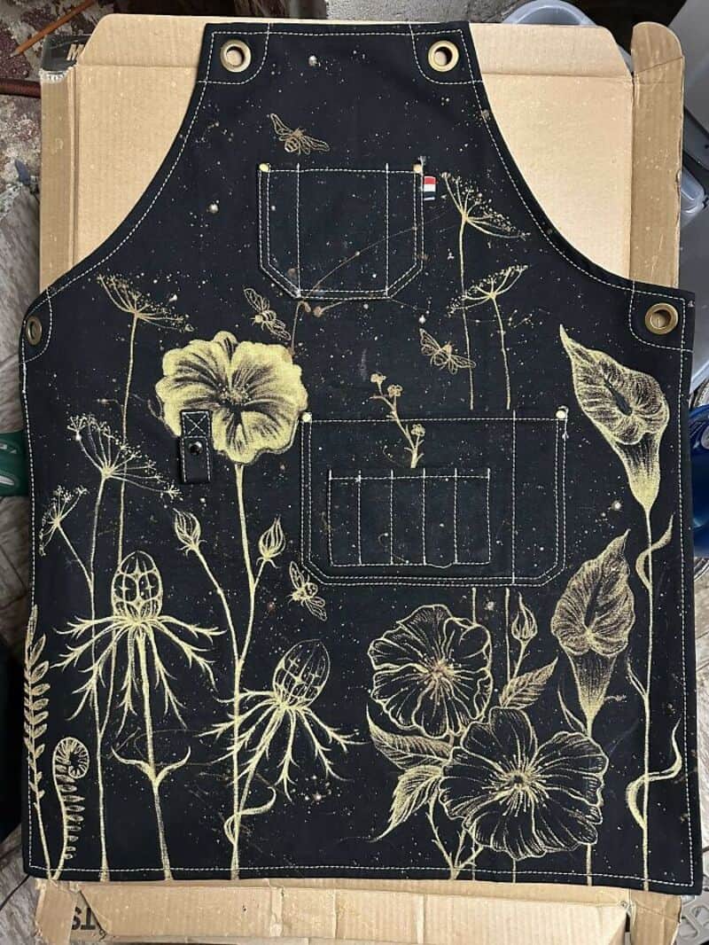 Black apron with yellow floral and insect design, front view.