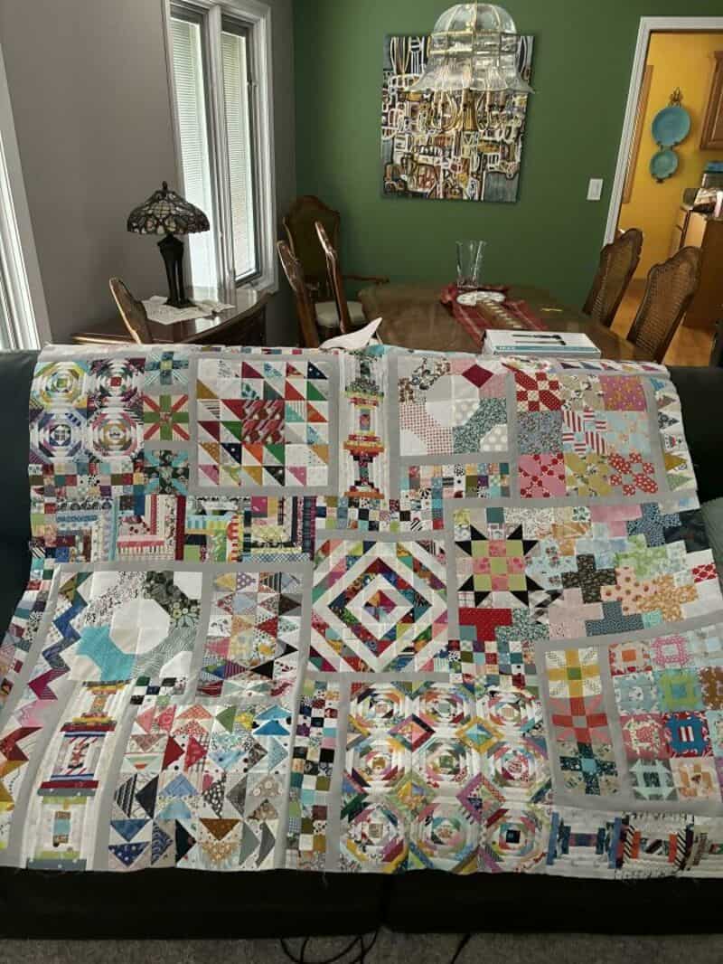 Colorful patchwork quilt covering a sofa in a dining room with green walls and a wooden table.